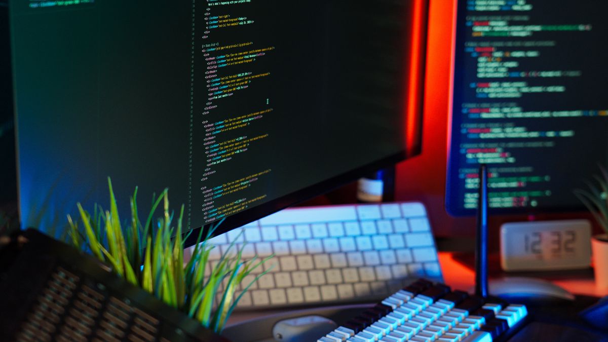 Developer workspace with dual monitors showing code and a keyboard—Kaneo vs Jira project management decision context