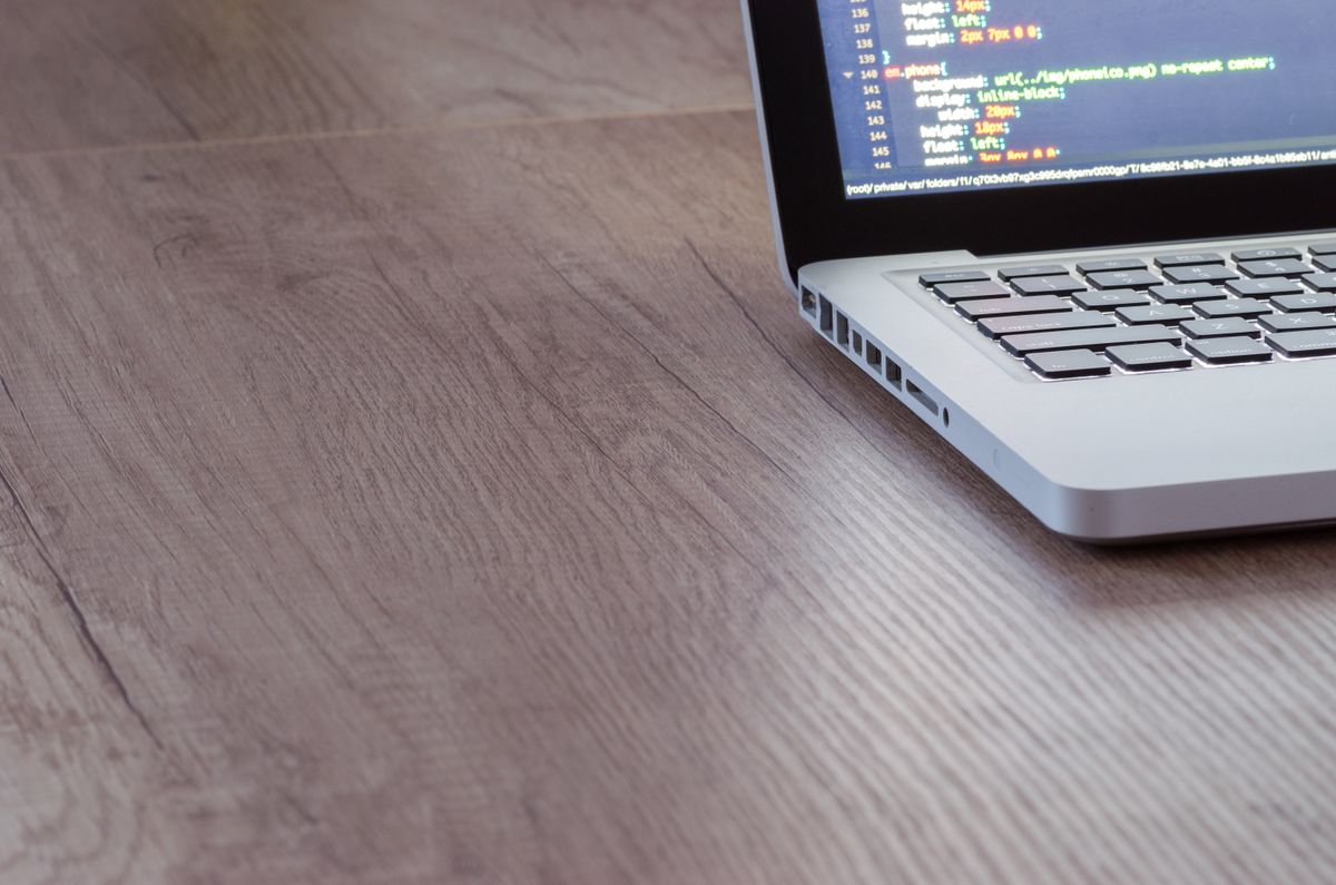 Mac laptop on a wooden desk displaying code in an editor—Claude Code Rules, Skills, and Workflow configuration context