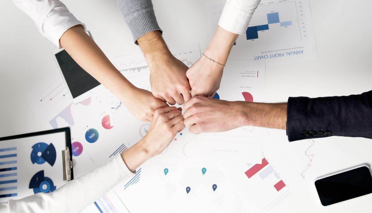Équipe en poignée de main collective au-dessus de graphiques imprimés sur une table de travail — choix Kaneo vs Jira