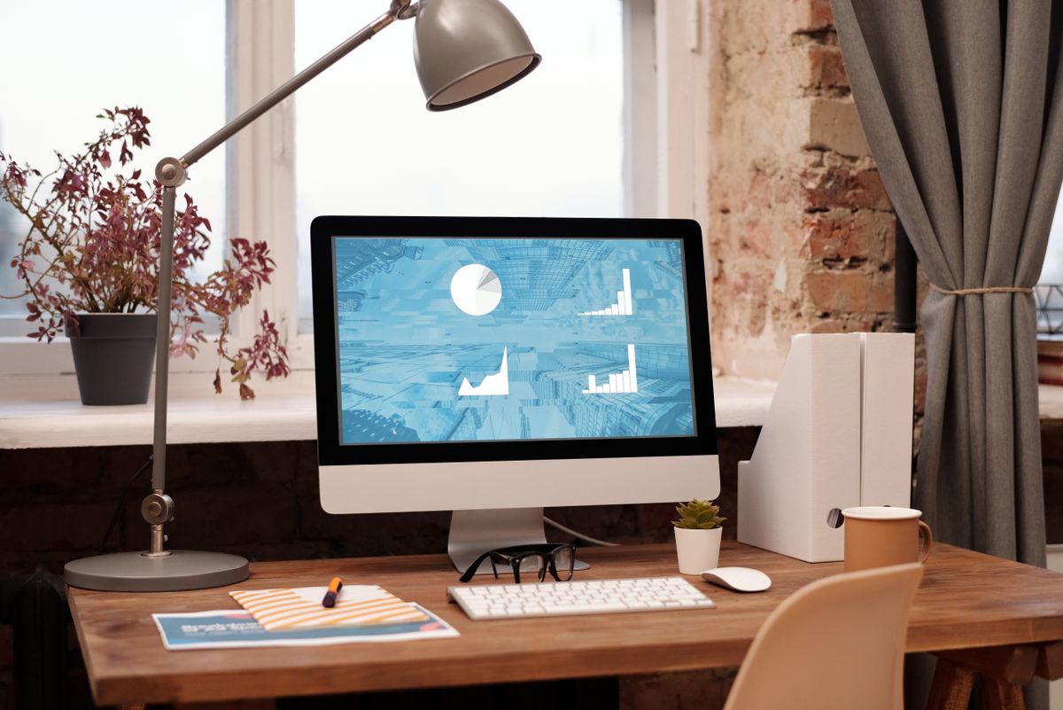 木質辦公桌上 iMac 顯示專案進度圖表，旁有鍵盤與筆記本——Kaneo vs Jira 專案管理選型場景