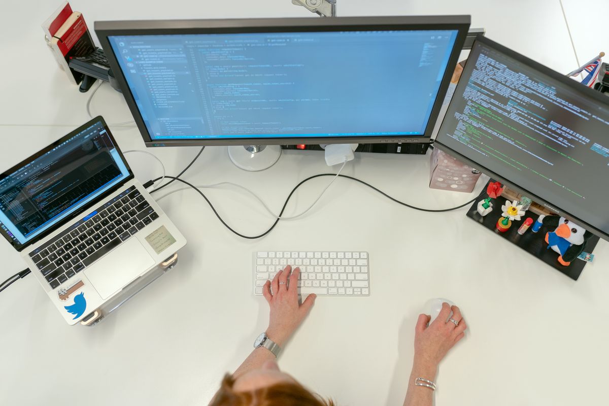 开发者俯拍多屏工作站，显示器上是代码与终端——Linux 服务器 SSH 远程排障场景